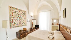 Camera d'albergo con un letto grande, una cassettiera, uno specchio, TV a parete e un arazzo decorativo.