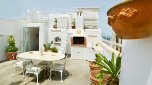 Una terrazza sul tetto con un tavolo rotondo e sedie, una zona barbecue e piante in vaso.