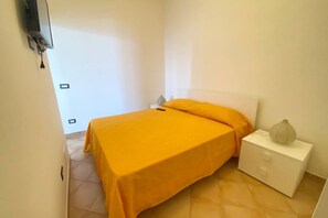 A small, bright room with a bed, a nightstand, and a television on the wall.