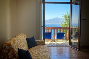 Una habitación con sofá, puerta corrediza de vidrio que da a un espacio exterior con vista a la montaña y al mar.