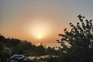 A sunset over a body of water with parked cars and trees in the foreground.