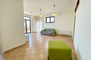 Une pièce spacieuse avec un canapé à motifs, un pouf vert et une fenêtre avec des rideaux.