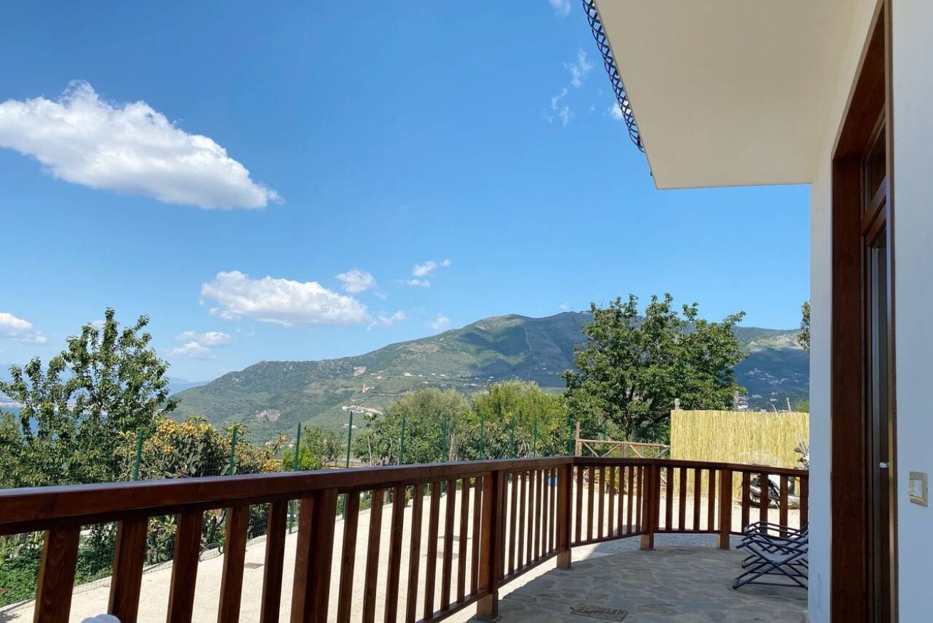 Un balcón con vista a montañas, barandilla de madera y una mesa con sillas.