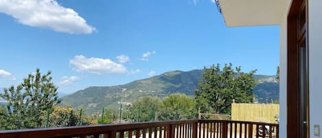 Un balcón con vista a montañas, barandilla de madera y una mesa con sillas.