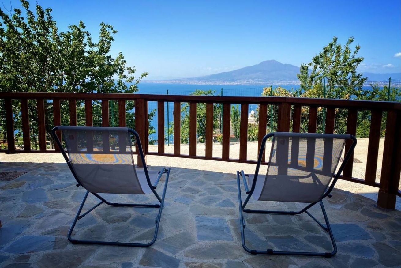 Two metal-framed lounge chairs on a stone patio with a view of a body of water and a distant mountain.