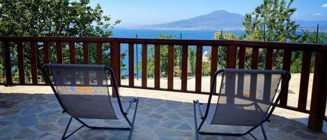 Two metal-framed lounge chairs on a stone patio with a view of a body of water and a distant mountain.