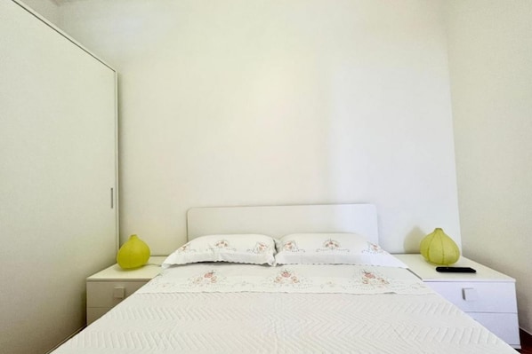 A single bed with a white headboard, two bedside tables, and a nightstand with a lamp.