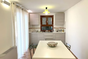 A kitchen with a white table, a window with curtains, and a ceiling light.