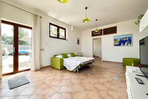 Een slaapkamer met een bed, een groene bank, een televisie en een schilderij aan de muur.