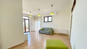 A spacious room with a patterned sofa, a green ottoman, and a window with curtains. - La Badia – Il Vigneto🌿 | Breathtaking View of Vesuvius and the Gulf of Naples (Vico Equense)
