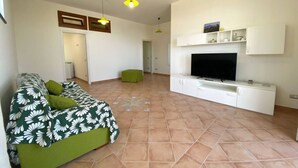 A living room with a green sofa, a flat-screen TV, white cabinets, and a tiled floor. - La Badia – Il Vigneto🌿 | Breathtaking View of Vesuvius and the Gulf of Naples (Vico Equense)