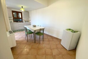Une cuisine de taille réduite comprenant une table à manger, des chaises, un réfrigérateur et une fenêtre avec des stores.