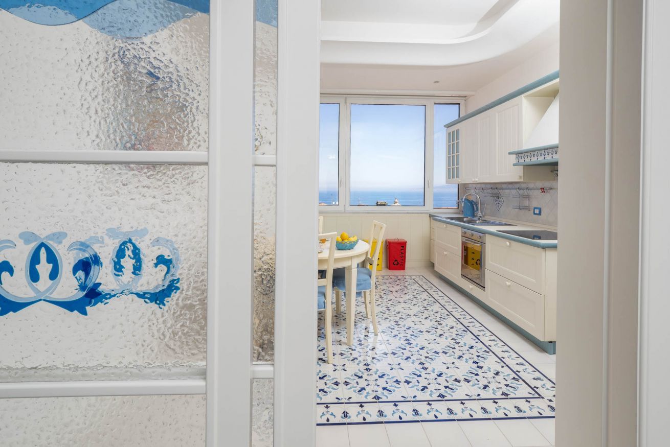 A kitchen with a view of the sea, a dining area with a table and chairs, and a patterned floor.
