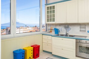 Eine Küche mit Blick auf eine Stadtlandschaft und ein Gebirge, mit weißen Schränken, einer blauen Arbeitsplatte und drei bunten Mülleimer.