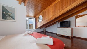 Une chambre avec un grand lit, des poutres apparentes en bois au plafond, une télévision et une fenêtre donnant sur un beau paysage.