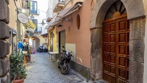 Une rue étroite où est garée une moto sur le bord, une porte en bois et un magasin avec une enseigne.