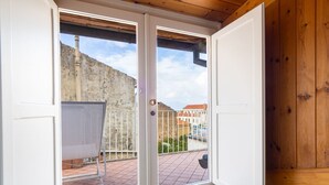 Une pièce dotée d’une porte-fenêtre coulissante donnant sur un balcon équipé d’un tableau blanc, offrant une vue sur un immeuble et possédant un plafond en bois.