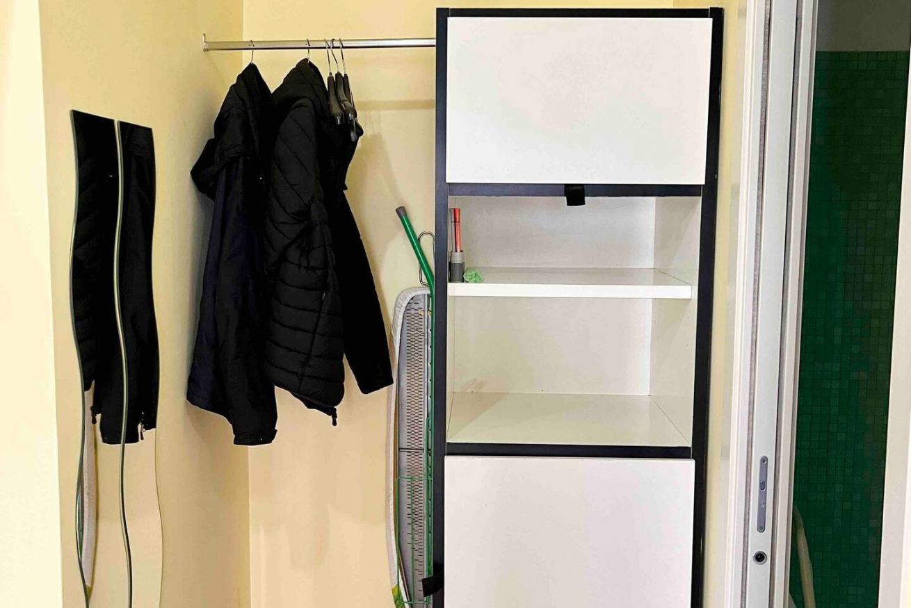 Ein Zimmer mit einem weißen Kleiderschrank, einer grünen Wand und einem schwarzen Jackett, das an der Wand hängt.