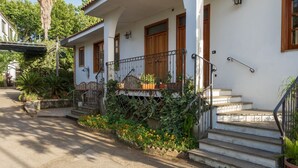 A white building with a porch, wooden doors, and a staircase leading to the entrance.