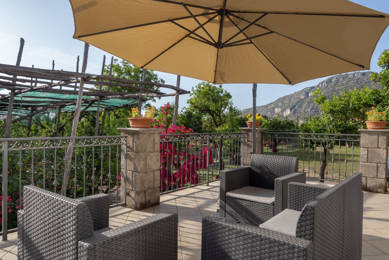 A patio with wicker furniture, a large umbrella, and potted plants.
