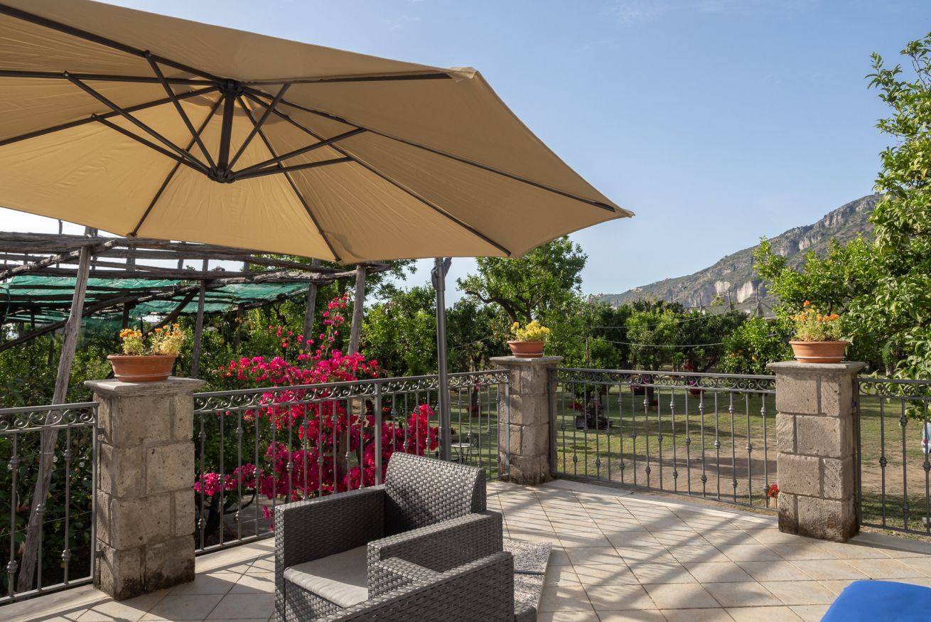 A covered patio with wicker furniture, a large umbrella, and potted plants.