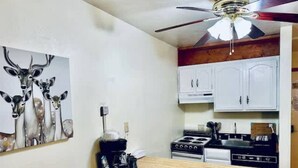 Une cuisine de taille réduite avec des meubles blancs, une cuisinière et un ventilateur de plafond.