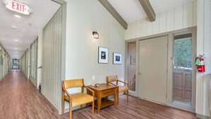 Un couloir doté d’un plancher en bois, une table avec deux chaises, des tableaux encadrés accrochés au mur et un panneau indiquant la sortie.
