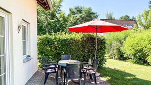 A patio with a table and chairs, a red umbrella, and a hedge in the background. - Wonderful private villa for 6 guests with WIFI, TV, terrace and pets allowed (Waren)
