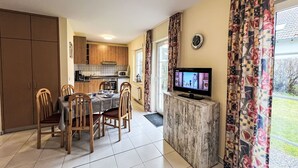 A compact kitchen with wooden cabinets, a dining table with chairs, a TV on a marble stand, and patterned curtains. - Wonderful private villa for 6 guests with WIFI, TV, terrace and pets allowed (Waren)