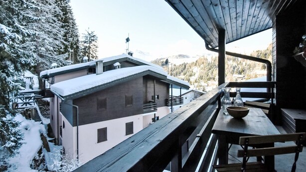 A wooden deck with a view of a building and snow-covered trees. - Beautiful apartment for 4 people with WIFI, TV and balcony (Madesimo)