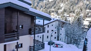 A modern building with a balcony, a car parked in front, and snow-covered surroundings with mountains in the background. - Beautiful apartment for 4 people with WIFI, TV and balcony (Madesimo)