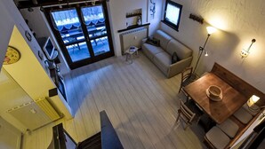 A cozy room with a wooden floor, a sofa, a table with chairs, a window with curtains, and a radiator. - Beautiful apartment for 4 people with WIFI, TV and balcony (Madesimo)