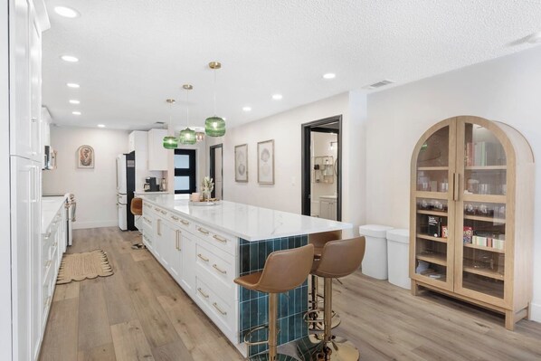A modern kitchen with a large island, bar stools, and a wooden cabinet with glass doors.