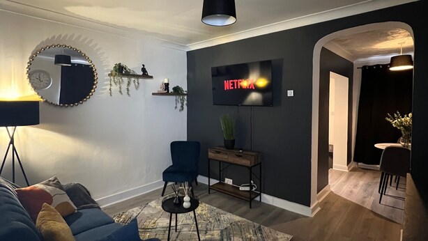 Una sala de estar moderna con un sofá azul, un espejo redondo, un televisor de pantalla plana y una mesa de centro de madera.