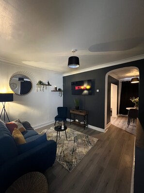 Un soggiorno moderno con un divano blu, uno specchio rotondo, una televisione a schermo piatto e un tavolino da caffè in legno.