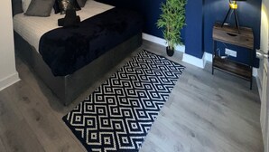 Un dormitorio con cama, un cuadro, una planta en maceta y una mesita de noche.
