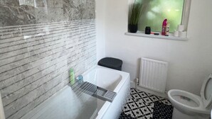 Un baño con bañera, inodoro y ventana con planta.