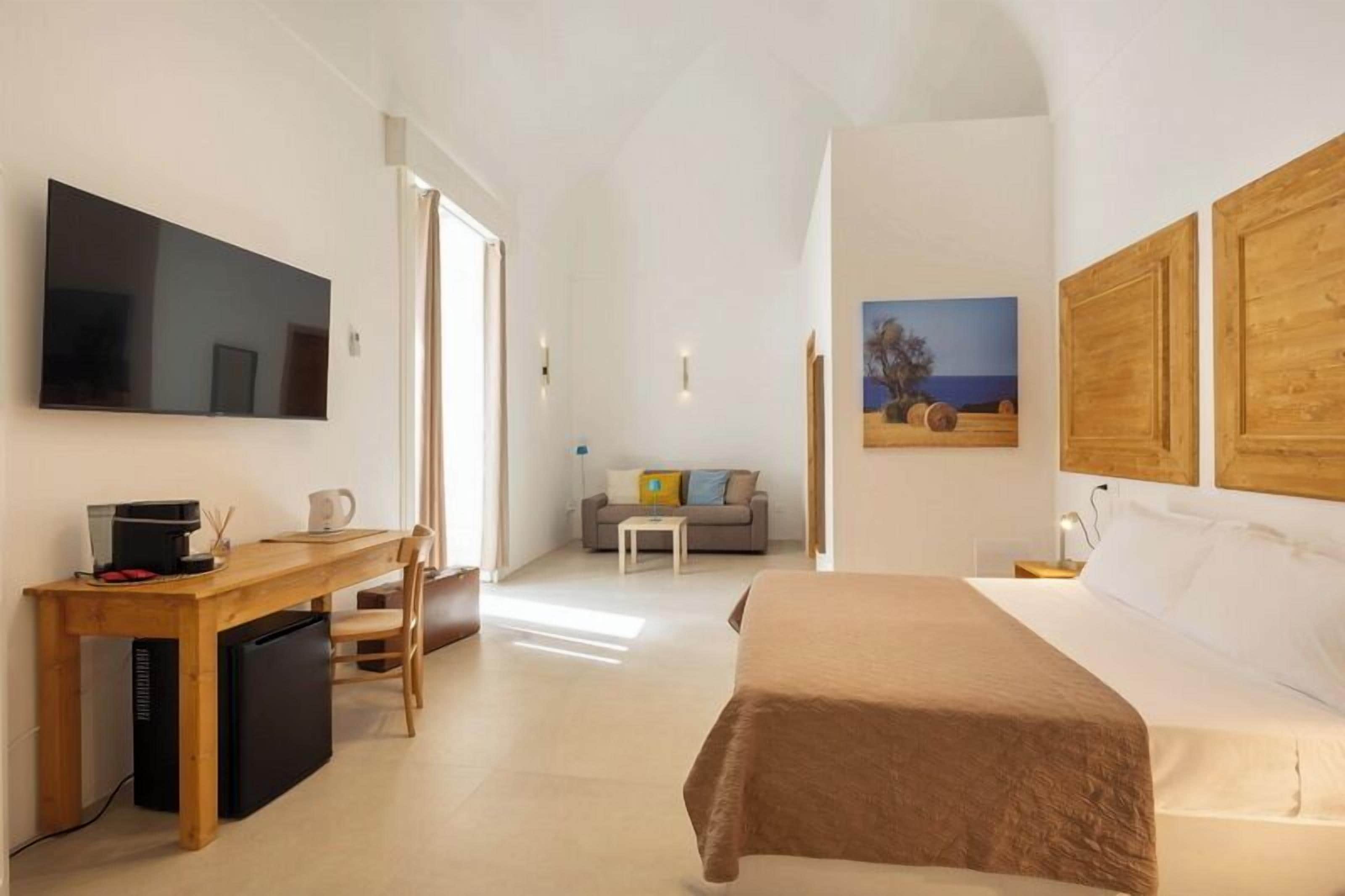 A bedroom with a bed, a desk with a computer, a TV, and a painting on the wall.