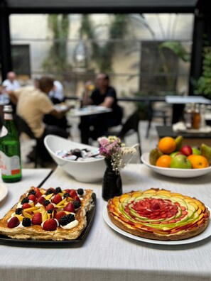 A dining table with two fruit-topped pastries, a bowl of fruit, and a bottle of drink. - Palazzo Kapece  (Monopoli)