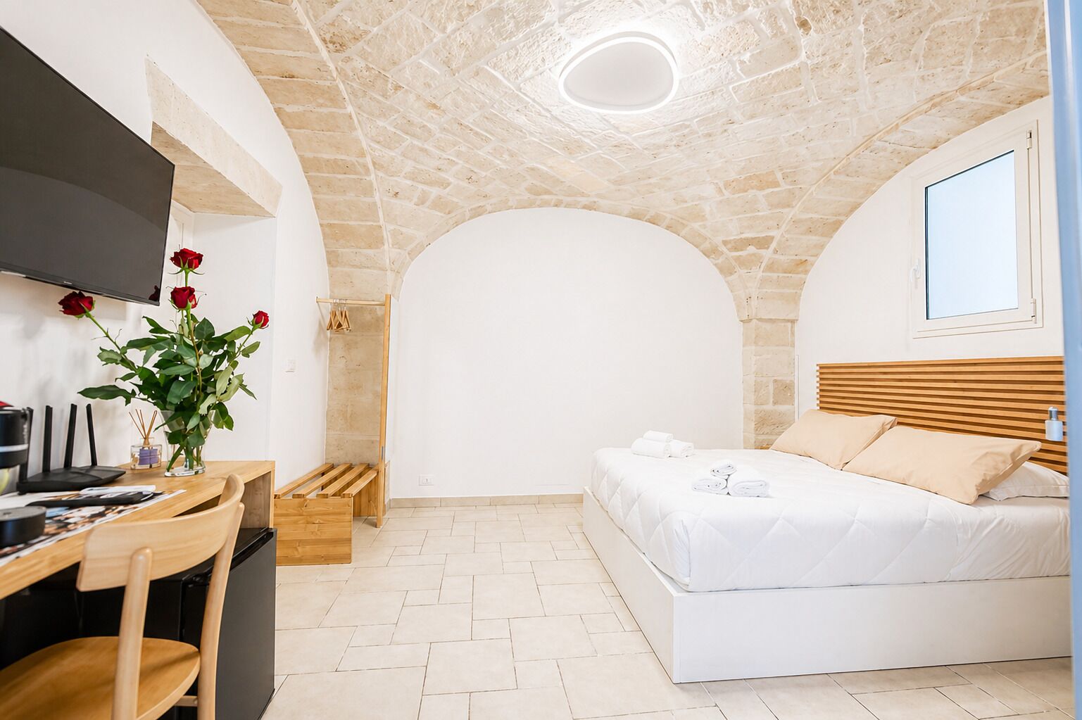 Ein Schlafzimmer mit einem Bett, einem Schreibtisch mit Stuhl, einem Fernseher und einer Vase mit Blumen.