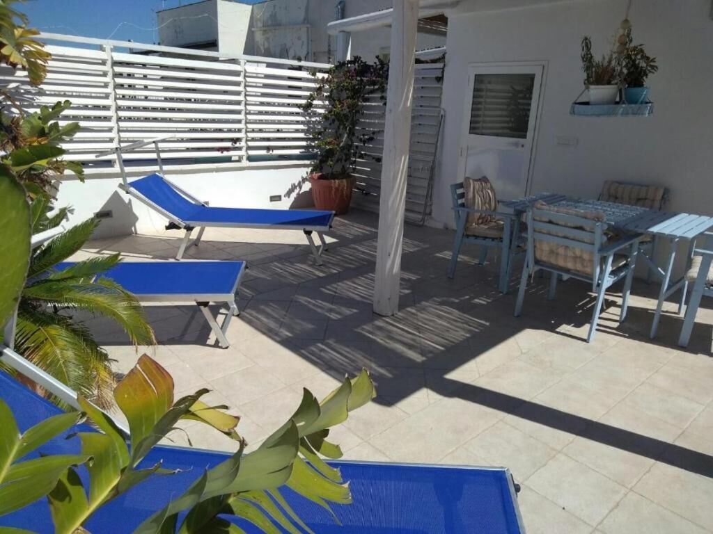 Eine Dachterrasse mit blauem Liegestuhl, einem Tisch mit Stühlen und Topfpflanzen.