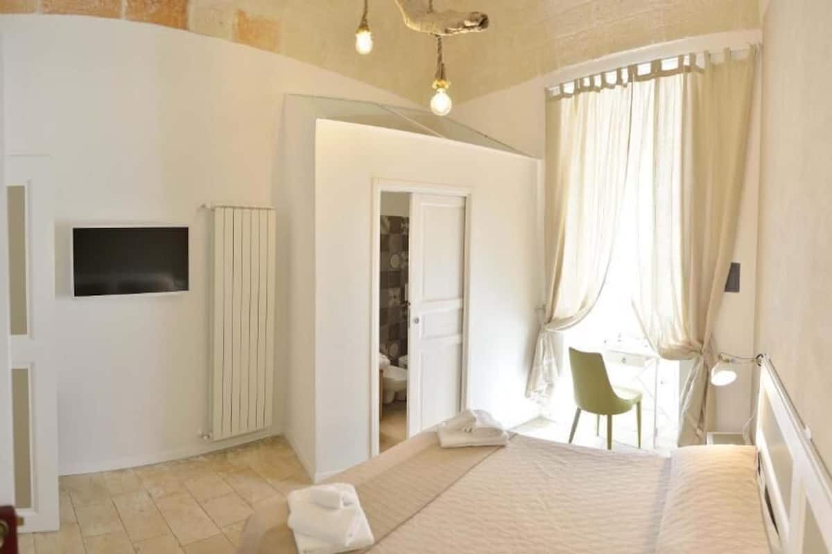 A bedroom with a bed, a TV, a desk, and a chair.
