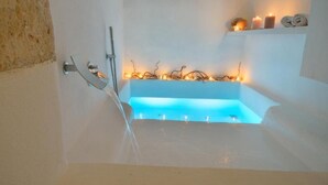 A modern bathroom with a bathtub, a shower, and a shelf with candles and a plant. - Palazzo Kapece  (Monopoli)