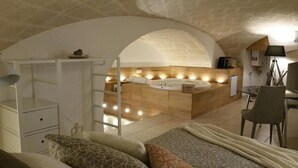 A bedroom with a large bed, a wooden vanity with a bathtub, and a desk with a chair. - Palazzo Kapece  (Monopoli)