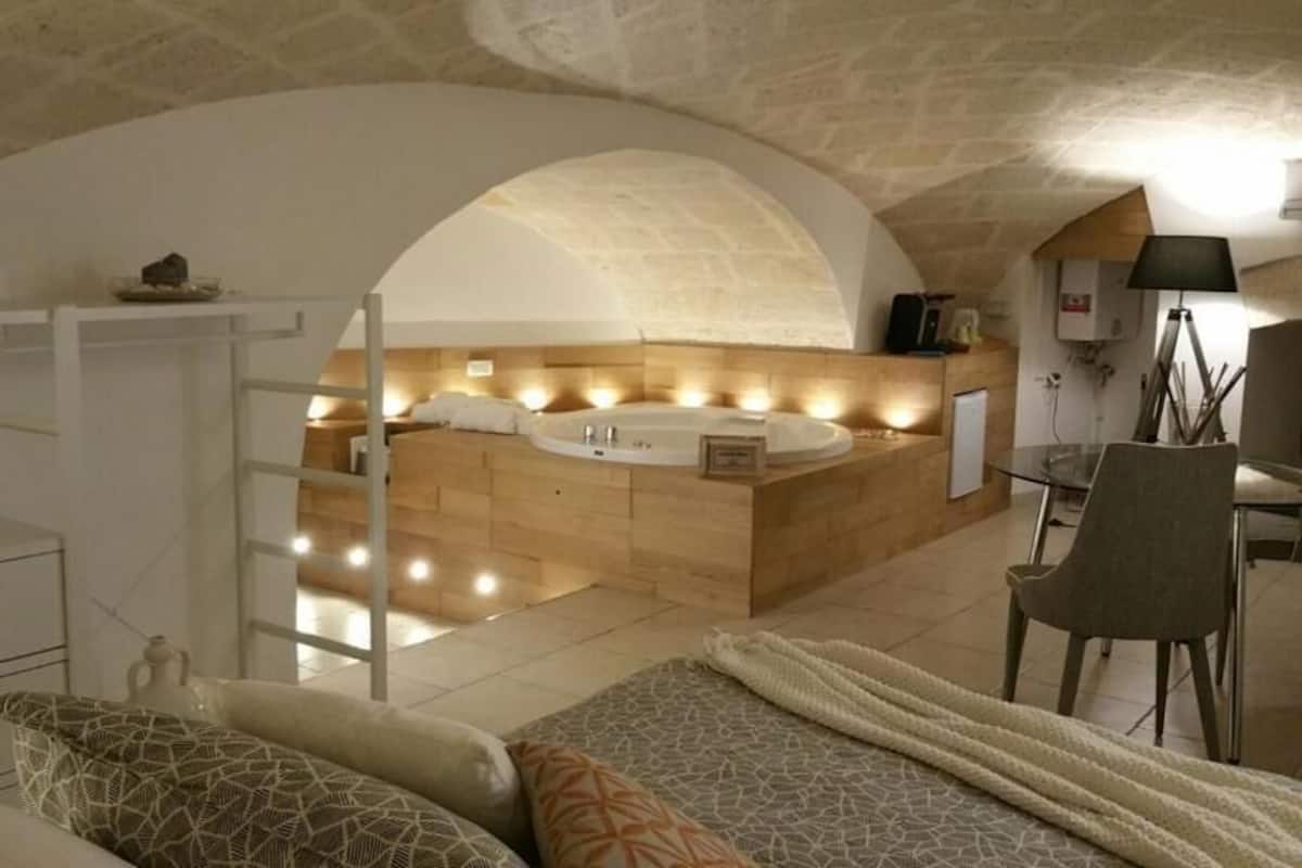 A bedroom with a large bed, a wooden vanity with a bathtub, and a desk with a chair.
