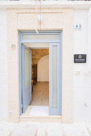 Entrada de um edifício com porta de vidro, arco de pedra e placa indicando 'Vico Gelso'.