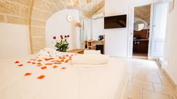 A hotel room with a stone ceiling, a bed with white linens, a TV on the wall, and a bathroom visible through an open door.