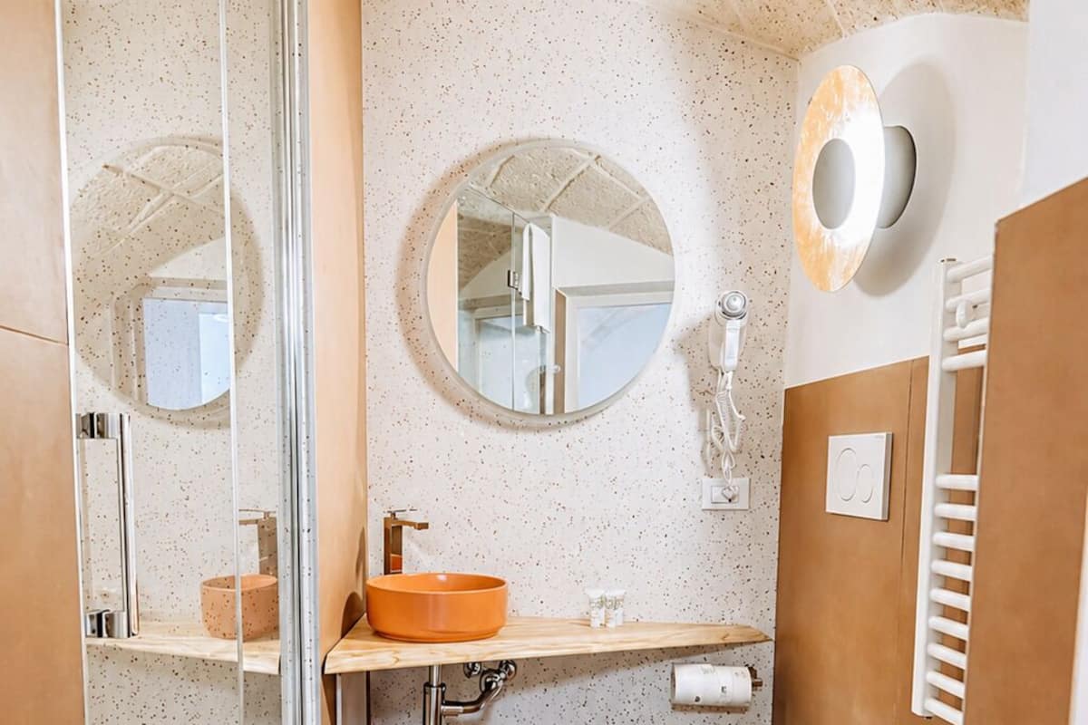 A modern bathroom with a glass shower enclosure, a round mirror, a wooden vanity, a white toilet, and a white sink.
