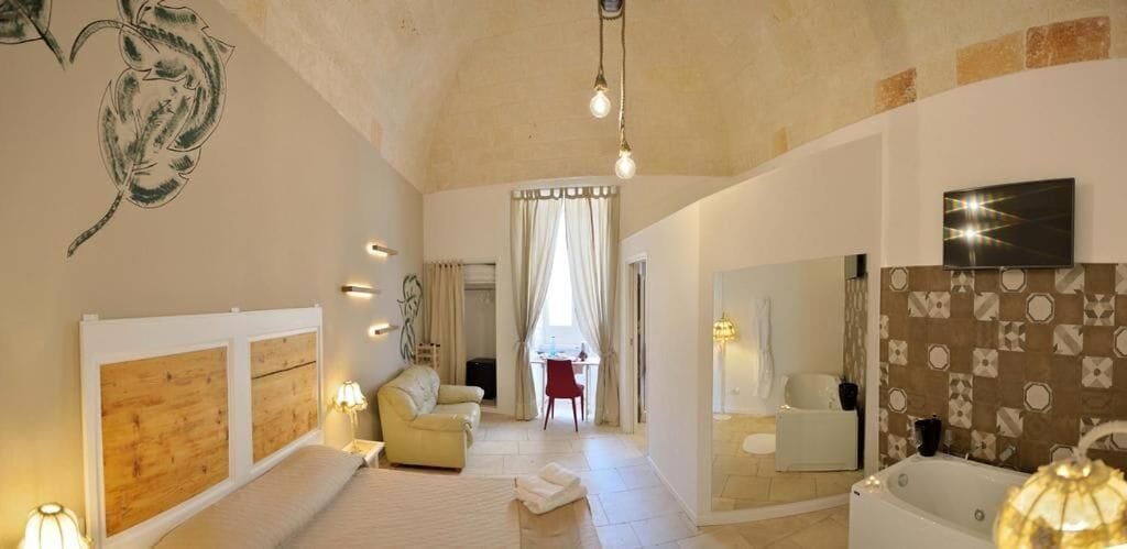 A spacious room with a large bed, a sitting area with a sofa, a dining table, and a bathroom with a bathtub and mirror.