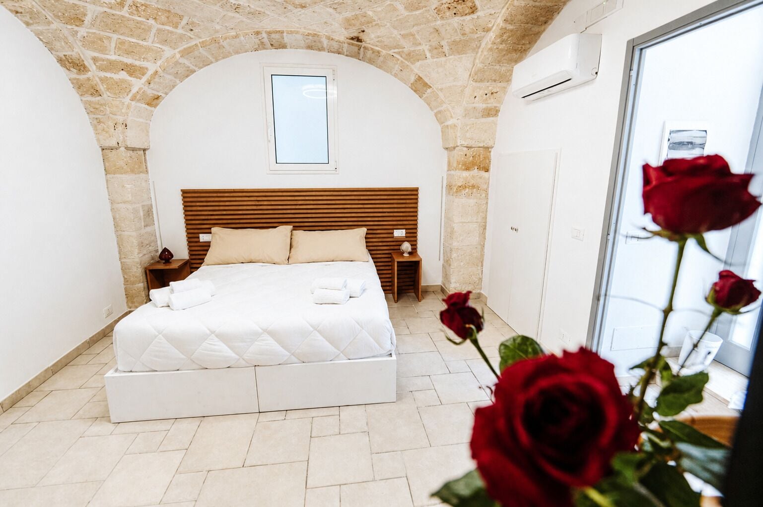 A bedroom with a stone arch ceiling, a wooden headboard, a bed with white bedding, a nightstand, and a window.